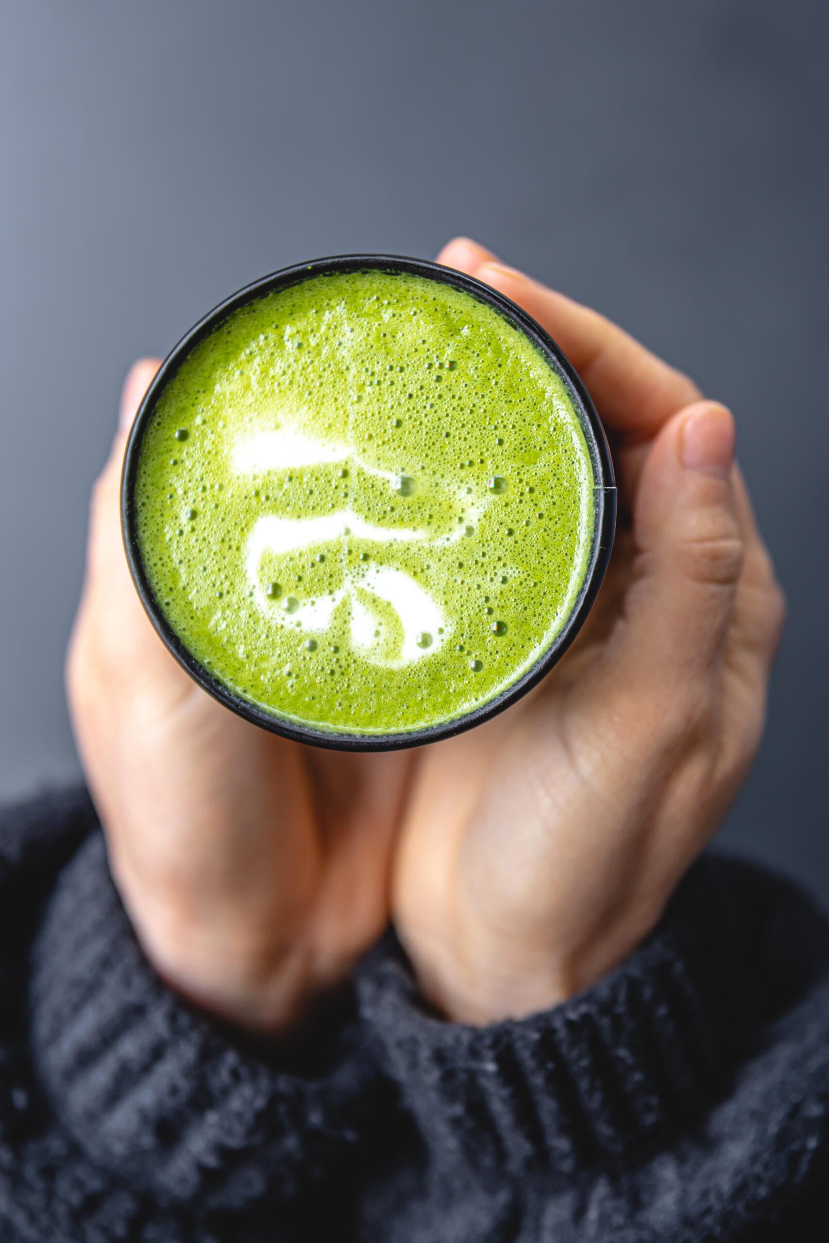 Top view of woman holding in hands trendy green matcha drink with latte art.